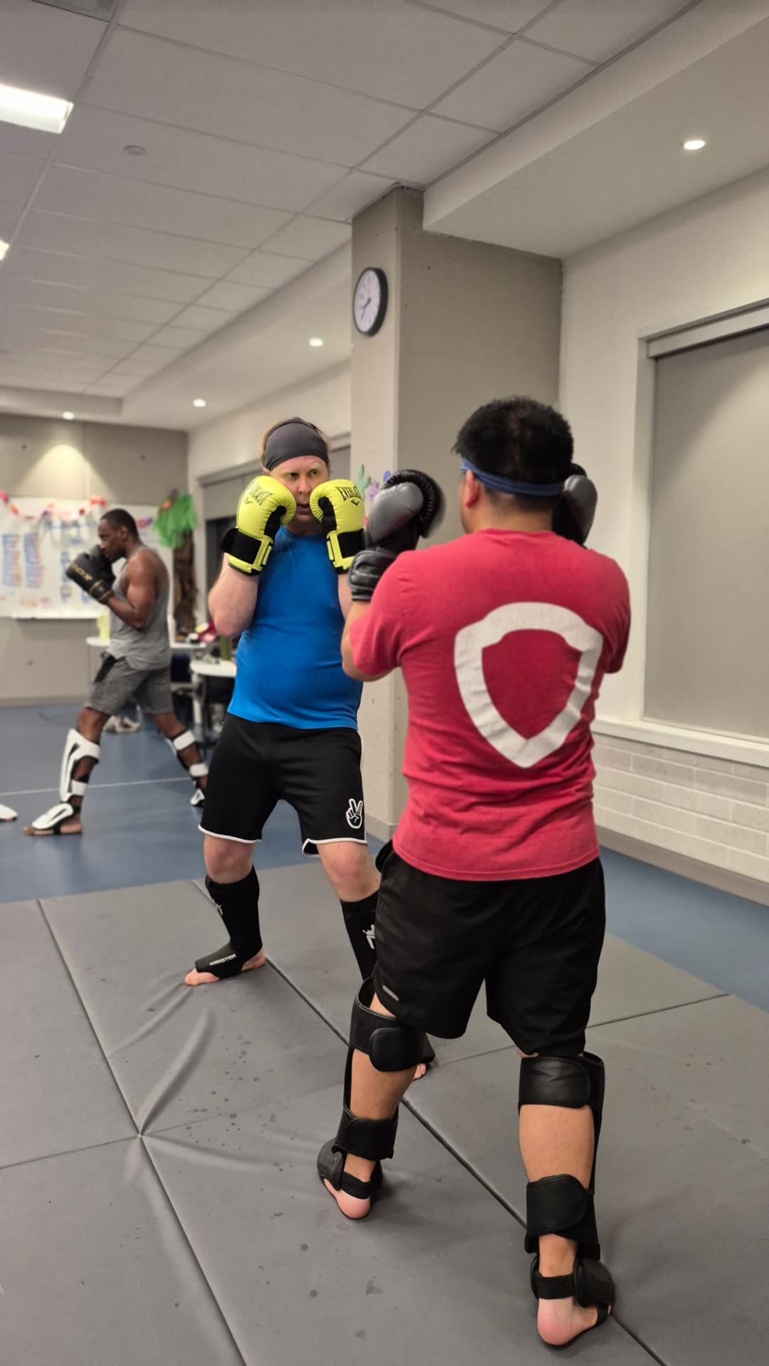 Two adult students spar in guard position wearing gloves and shin pads