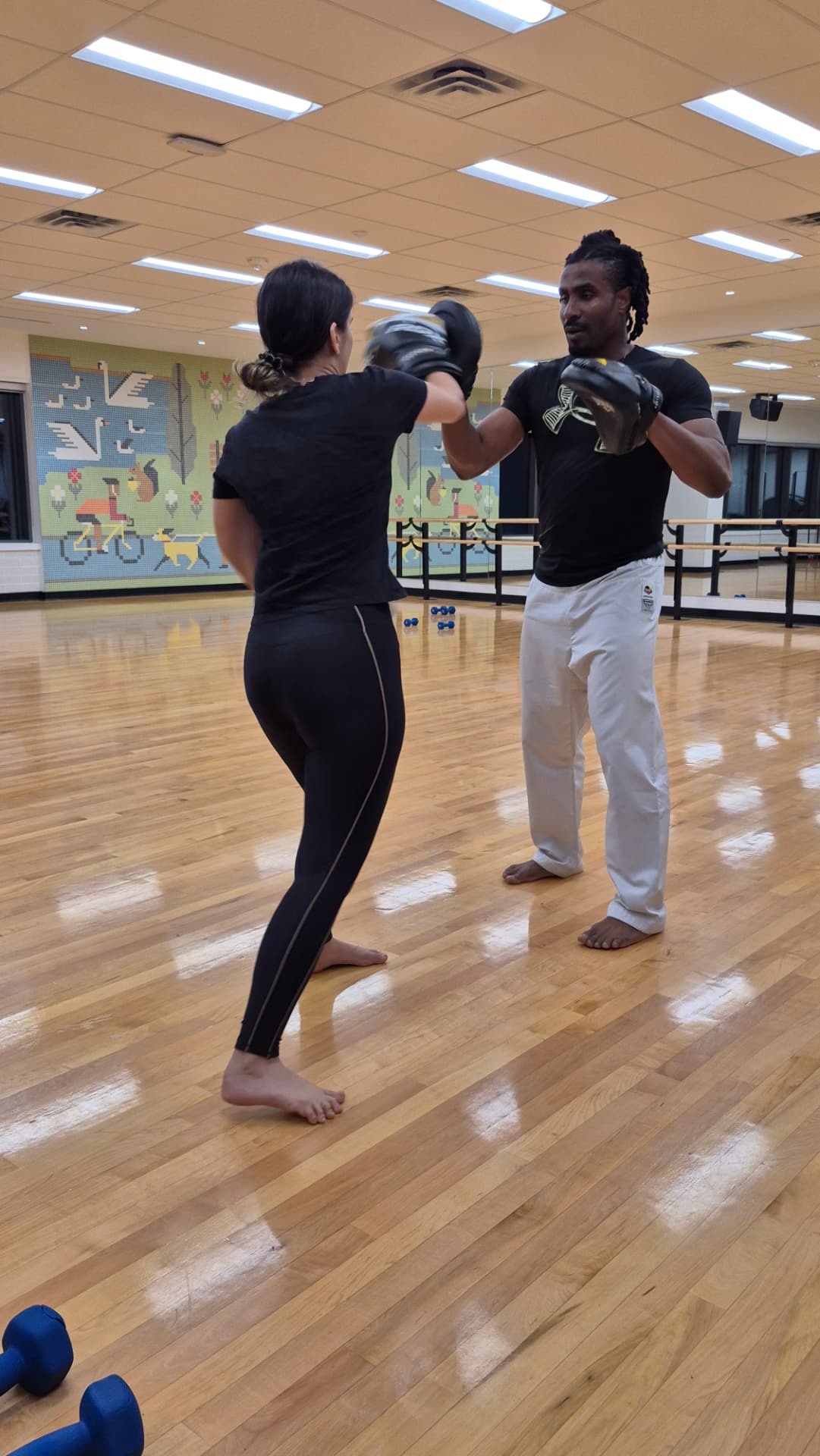 An adult student lands a straight punch on the instructor's mitt during class