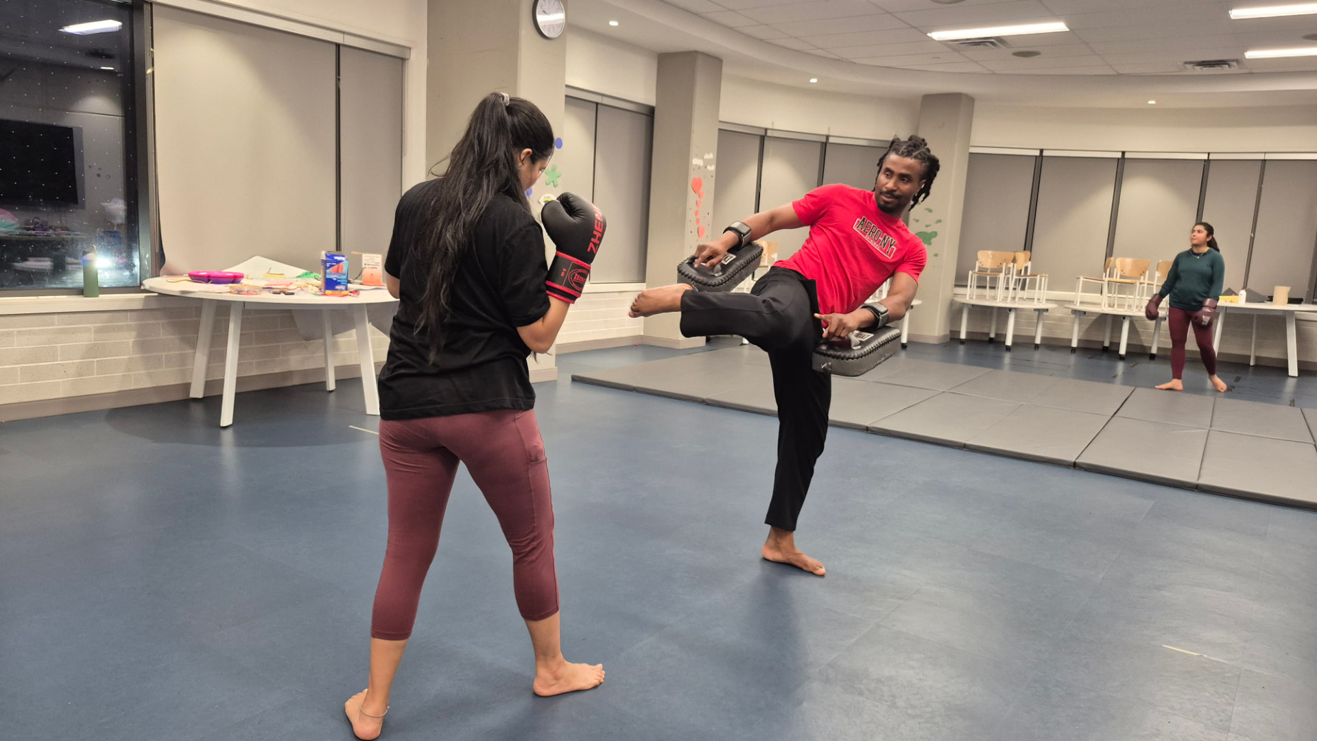 An instructor holds pads while an adult student throws a kick during a kickboxing drill