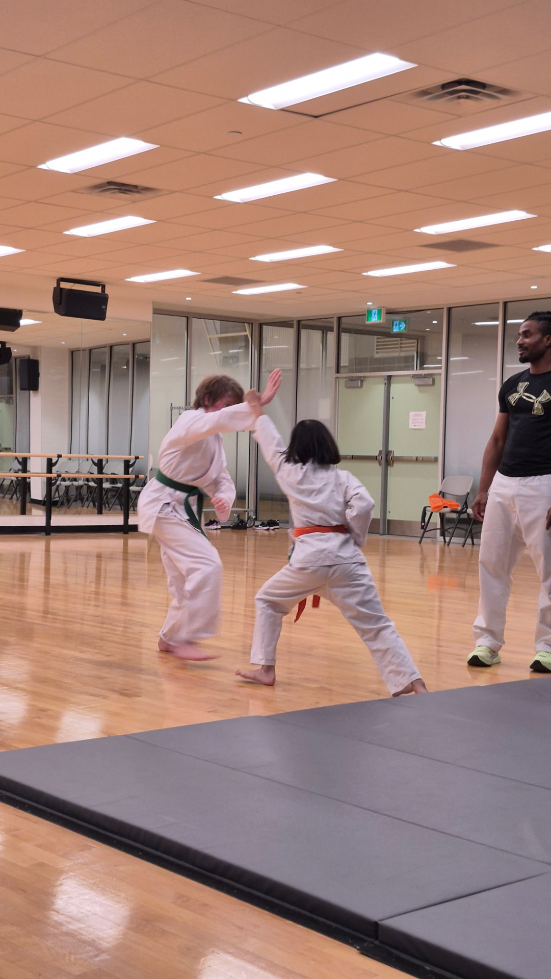 An instructor observes two children practising a karate drill together in a dojo