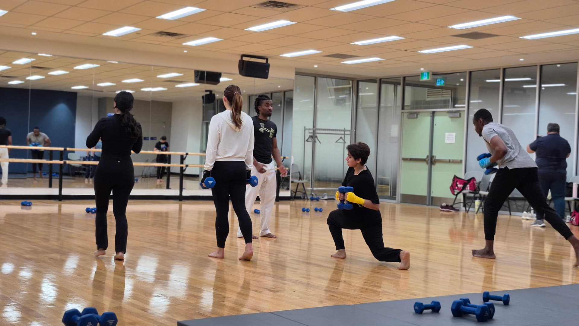 Adults train conditioning with dumbbells in a studio kickboxing session