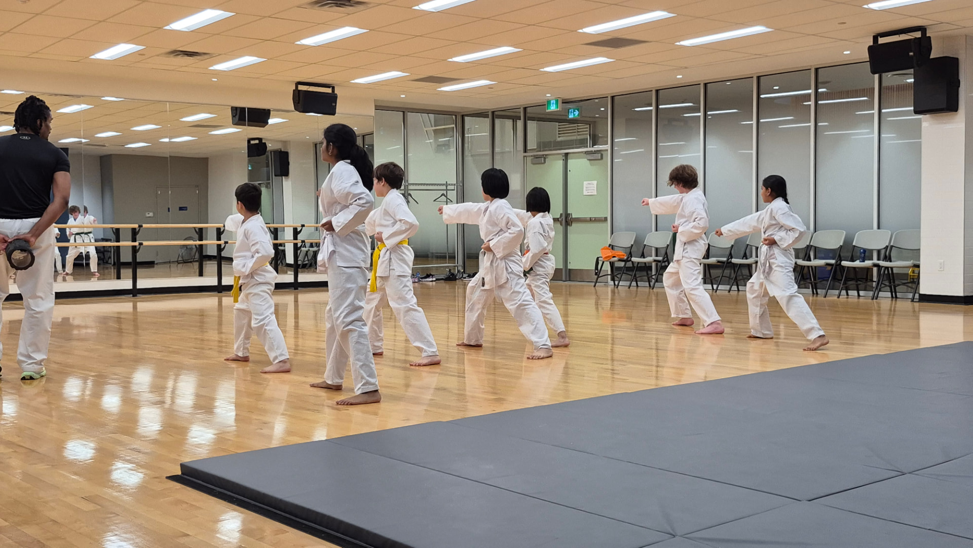 Children in white karate gi practise stances in a line across a bright dojo