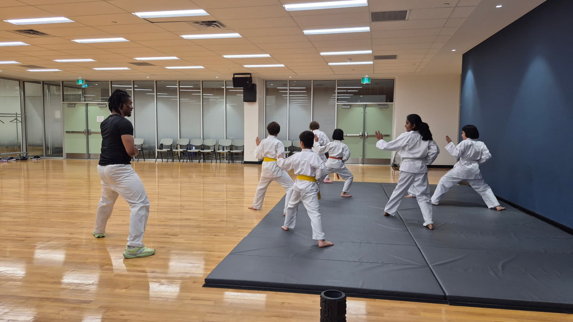An instructor leads a group of children in karate stances on wooden floors