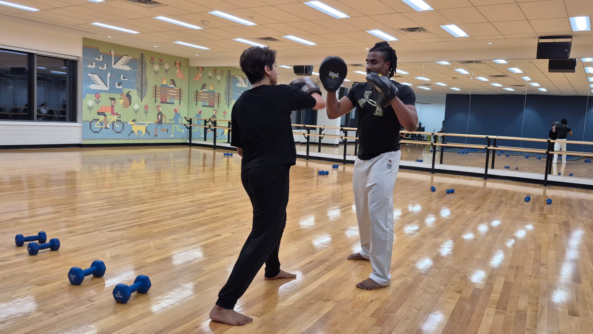 An adult student works pad rounds one-to-one with the instructor in a mirrored studio