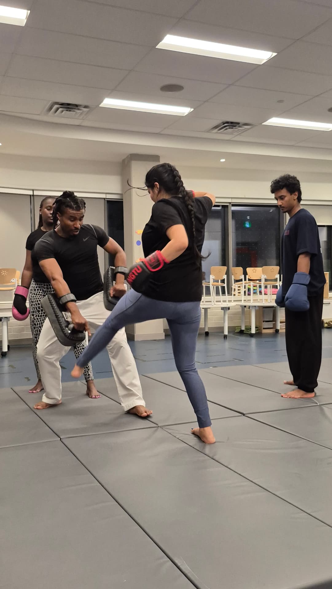 An adult kickboxer drives a knee strike into pads during class