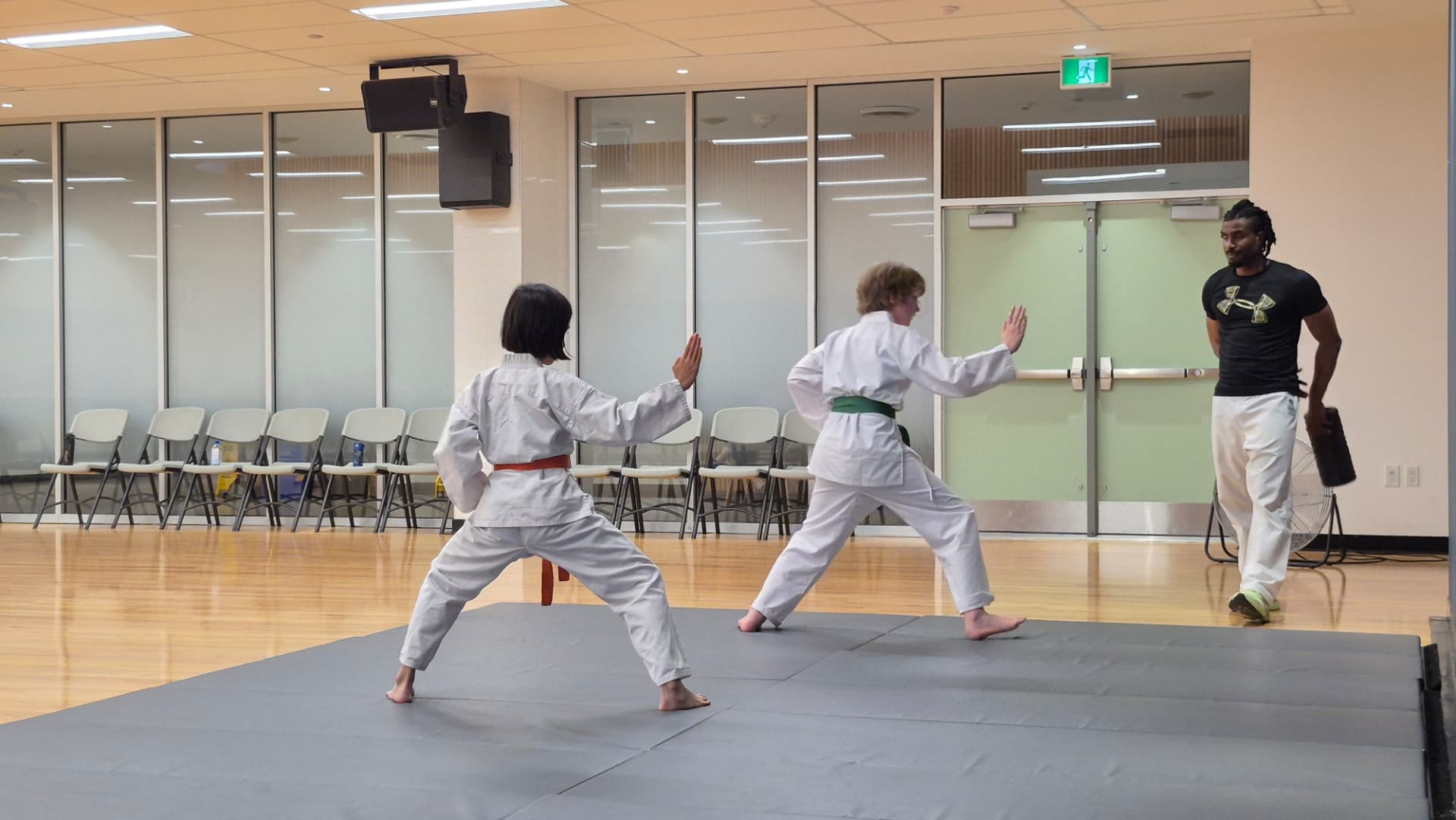 Two young karate students practise stances while their instructor observes